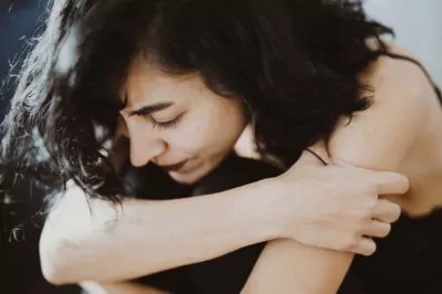 Close-up of a woman with dark hair hugging her knees, conveying a sense of introspection and emotional reflection.