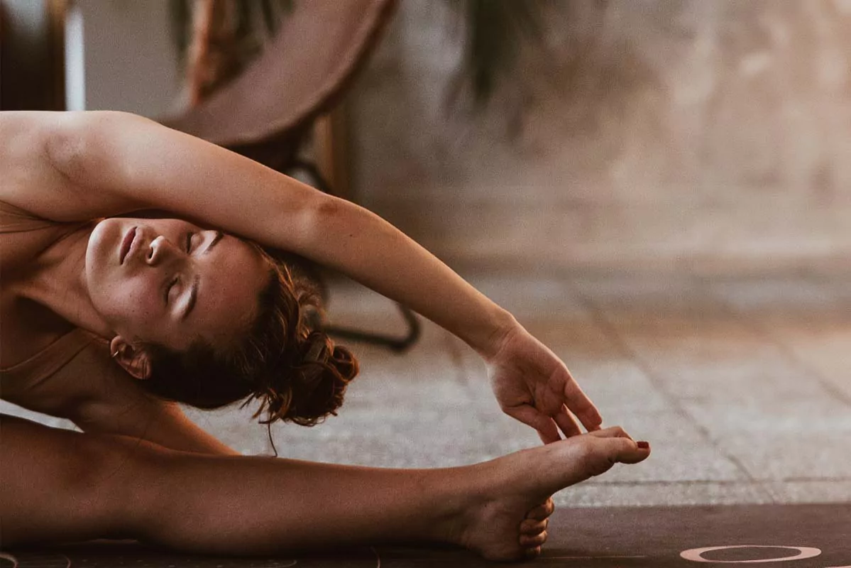 Young woman performing a yoga stretch on a mat, focusing on flexibility and relaxation.