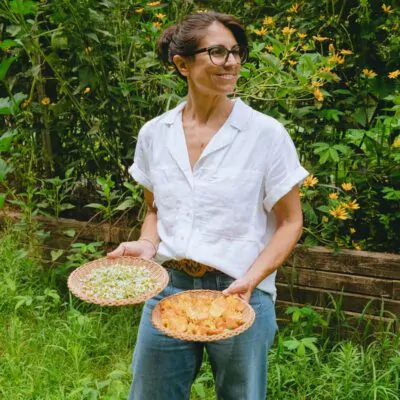 Annmarie holding baskets of harvested herbs in her garden